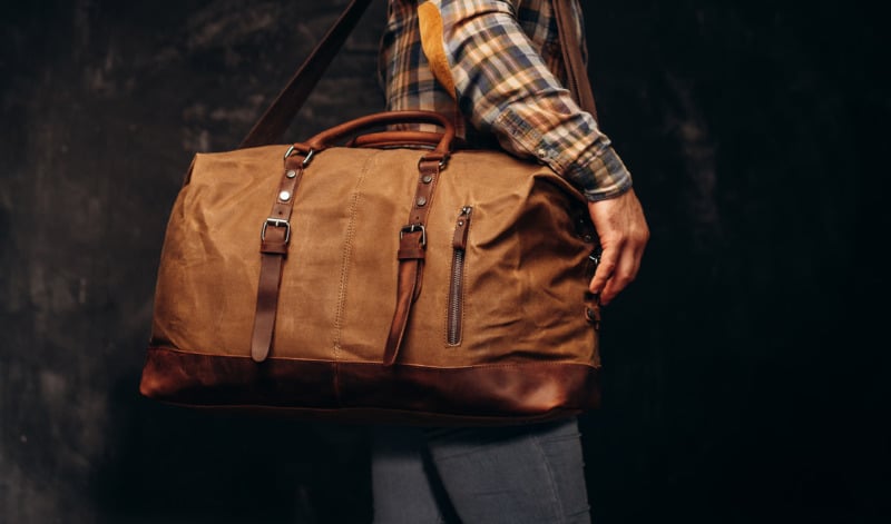 Man wearing a black and brown flannel carrying a brown duffel bag