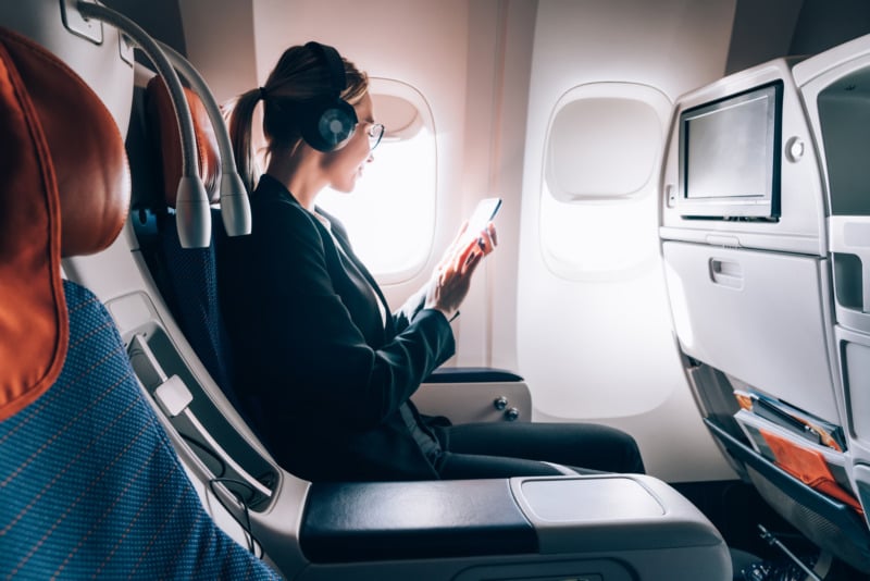 Caucasian female airplane passenger wearing a headphone and using phone